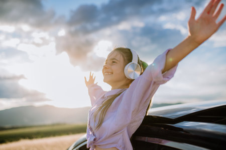 Little girl with headphones standing and leaning out of the car window during the ride.の写真素材