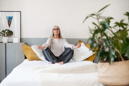 Senior woman doing yoga and meditating on her bed.の写真素材