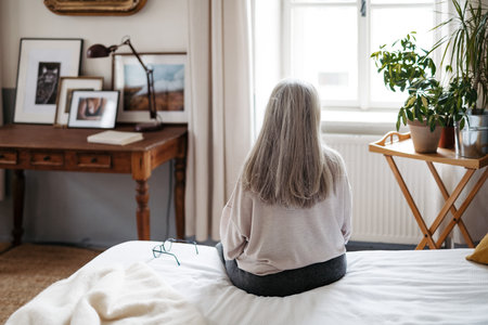 Rear view of senior woman sitting on a bed.の写真素材