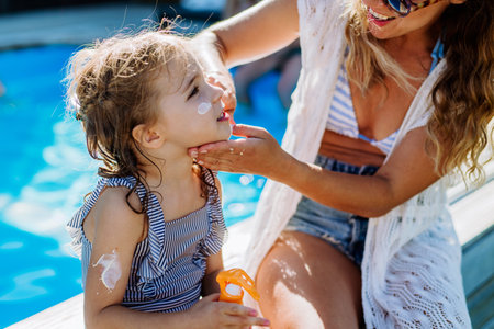 Young mother applying sunscreen lotion to her daughter. Safety sunbathing in hot day.の写真素材