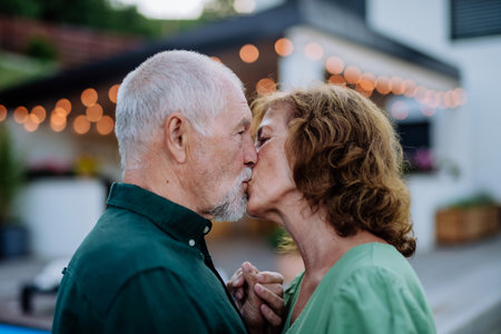 Senior woman and man dancing and kissing together in a garden in summerの写真素材