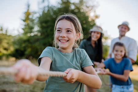 Young family with happy kids having fun together outdoors pulling rope in summer nature.の写真素材