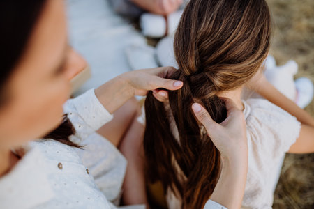 Close-up of mother making hairstyle to her daughter during family picnic in nature.の写真素材