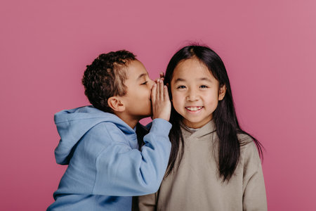Portrait of little boy whispering something to his friend.の写真素材
