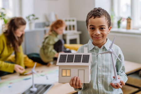 Little boy posing with model of wind turbine and model of house with solar system during a school lesson.の写真素材