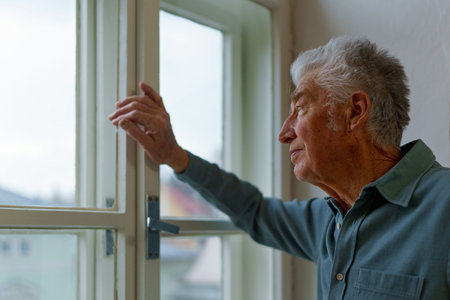 Senior man looking out of window, concept of solitude in retirement.の写真素材