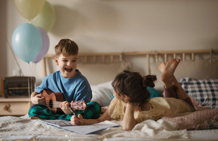 Little boy plaing on the guitar, while his sister drawing a picture.の写真素材