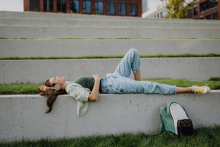 Young woman resting in city park with closed eyes, enjoying music trough headphones.の写真素材