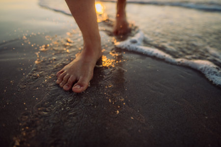 Woman walking on a beach during sunset, close-up of feet.の写真素材