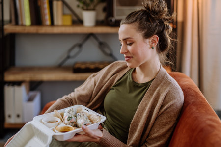 Young woman enjoying delivered food in her living room.の写真素材