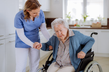 Nurse helping senior woman to stand up from wheelchair.の写真素材