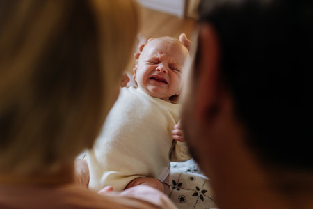 Close-up of parents cuddling their newborn crying baby.