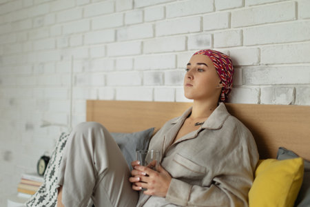 Young woman with cancer drinking water and lying in her bed, cancer awareness concept.の写真素材