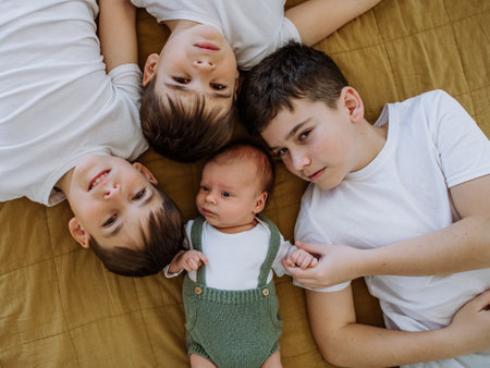Three big brothers with their little newborn brother lying in bed.の写真素材