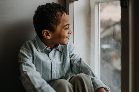 Little multiracial boy looking out of window.の写真素材