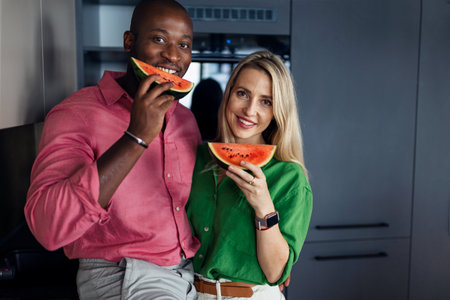 Multiracial couple eating melon in kitchen during hot sunny days.の写真素材