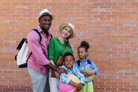 Multiracial family travelling together with small kids. Posing with beach ball in front of brick...
