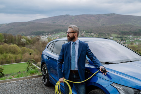 Mature businessman holding power supply cable from his electric car.