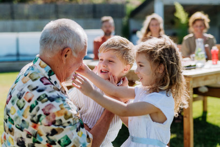 Little children having fun with their grandfather at outdoor family party.の写真素材