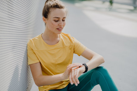 Young woman checking smartwatch in city, preparing for run, healthy lifestyle and sport concept.の写真素材