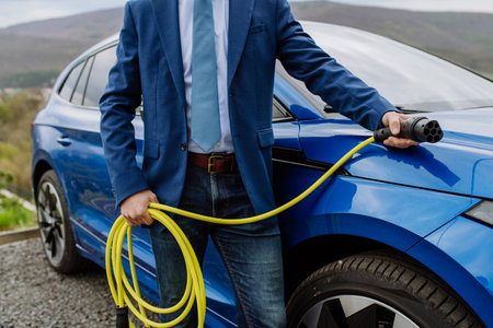 Close up of businessman holding power supply cable from his electric car.の写真素材