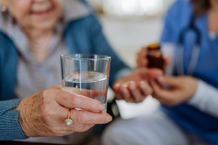Close-up of nurse giving medicine to senior woman at her home.