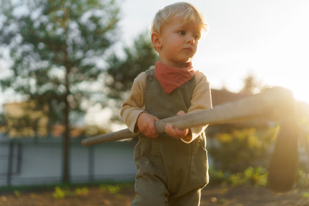 Little boy with hoe working in garden during autumn day.