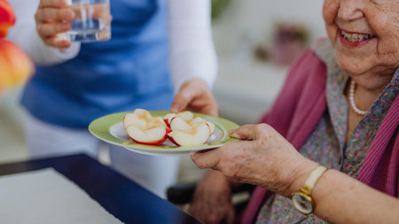 Nurse giving fruit snack to senior woman.の写真素材