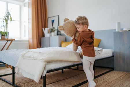Little boy cuddling with bear toy in bedroom.の写真素材