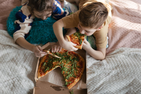 Top view of friends lying on a bed and eating pizza.の写真素材