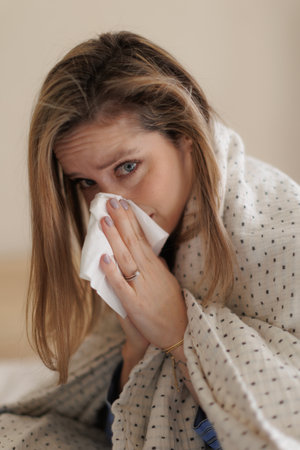 Portrait of young sick woman sneezing at bedroom.