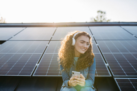 Portrait of young excited woman on roof with solar panels, listening music.の写真素材