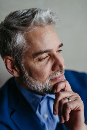 Handsome man with gray hair and beard smiling, looking aside studio portrait on gray copy space.の写真素材