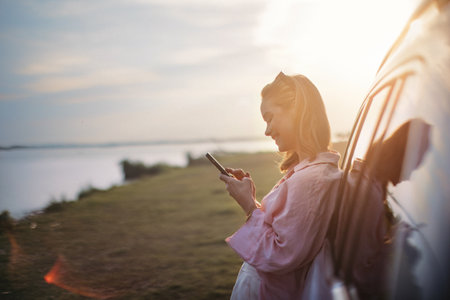 Young woman scrolling phone, leaning on her car in nature,の写真素材