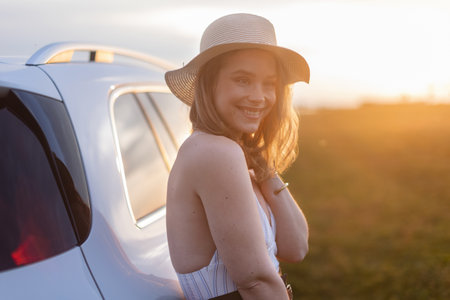 Portrait of young smiling woman standing near her car, enjoying summer time.