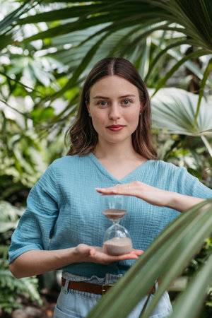 Young woman with hourglass in jungle, concept of nature protection.