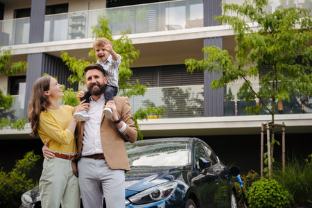 Happy family standing in front their electric car and charging it on the street.の写真素材