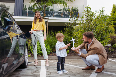 Happy family standing beside their car and charging electric car on the street.の写真素材