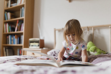 Cute little girl reading book lying on bed.の写真素材