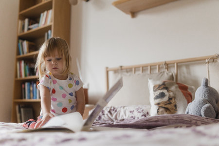 Cute little girl reading book lying on bed.の写真素材