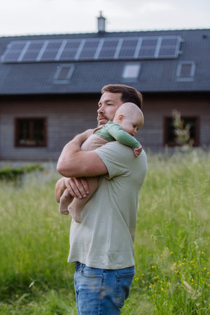 Happy father with baby standing in front of their house with solar panels.の写真素材