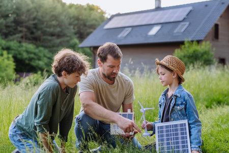 Father and his children holding solar panl standing in front of their house with photovoltaics on the roof.の写真素材