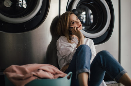 Young woman calling, waiting in a laundry room.の写真素材