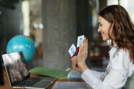 Close up of young woman holding plane tickets, having online call.の写真素材