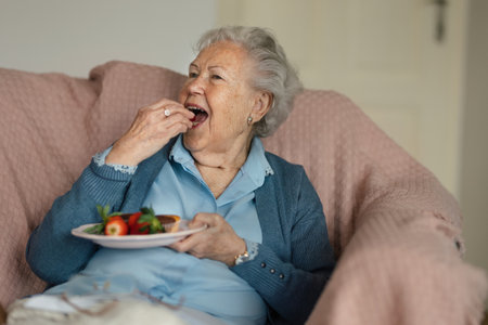 Senior woman resting at home and eating strawberries.の写真素材