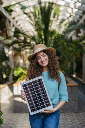 Young woman in botanical garden holding solar panel, concept of green energy.の写真素材