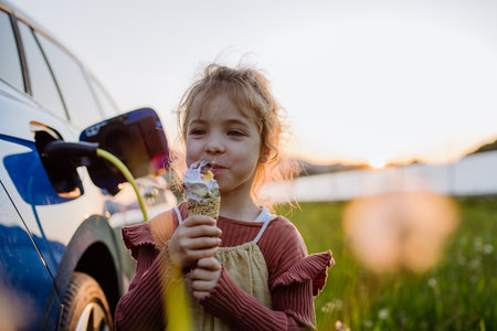 Little girl eating ice cream while charging their electric car.の写真素材