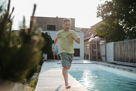 Young boy running along swimming pool at home.の写真素材