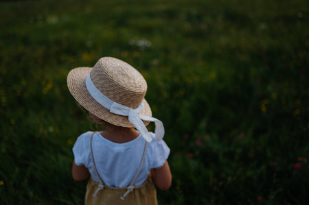 Rear view of adorable little girl with straw hat standing in the middle of summer meadow.の写真素材