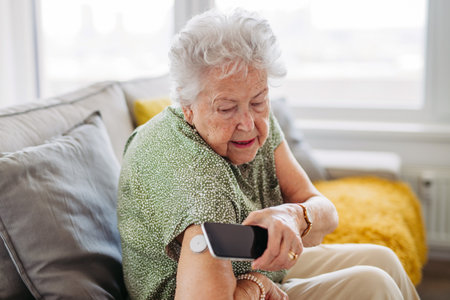 Diabetic senior patient checking blood glucose level at home using continuous glucose monitor.の写真素材